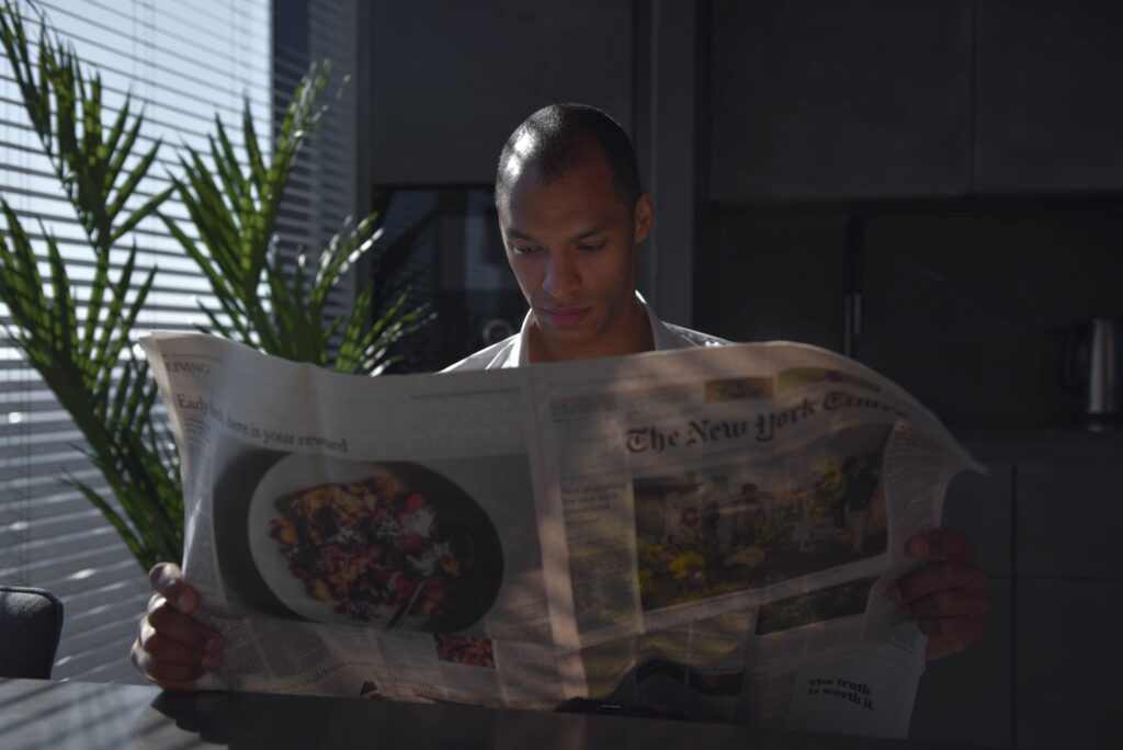 Businessman focused on reading newspaper in a sunny indoor office setting.